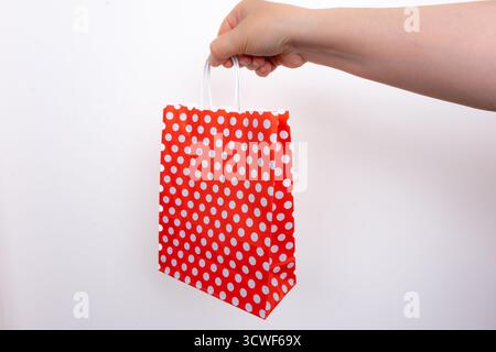 Hand holding red polka dot gift bag on isolated white background. Person gripping red dotted shopping bag. Gift and celebration concept Stock Photo