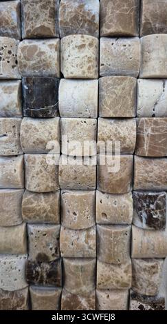 Photo of a wall covered in small, rectangular stone tiles with rounded edges. The stones display a variety of natural beige, cream, tan, and brown ton Stock Photo