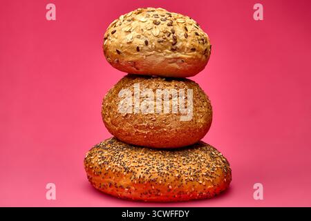 Artistic stack of three assorted bread rolls with seeds and grains on a vivid pink backdrop. A conceptual bakery still life emphasizing balance, fresh Stock Photo