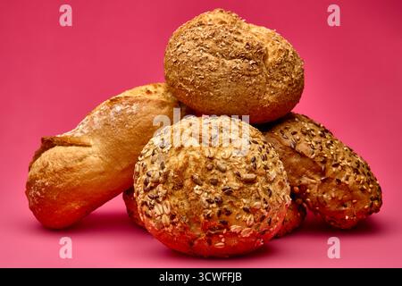 Assorted fresh bread rolls of various shapes and grains stacked together on a vivid pink background. Artistic food composition ideal for bakery advert Stock Photo