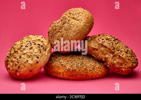 Creative composition of three bread rolls with grains and seeds arranged together on pink background. Fresh bakery still life perfect for healthy food Stock Photo