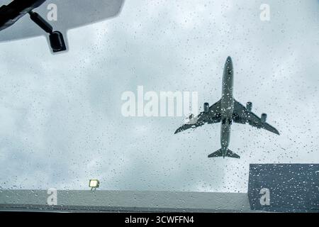 Miami Florida, commercial jet airplane approaching landing, view from inside car windshield, raindrops water droplets on glass, storm clouds dark sky, Stock Photo