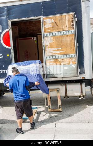 Miami Beach Florida, furniture delivery service, mover pushing padded wrapped sofa on dolly, worker in blue shirt unloading from truck, Latin Hispanic Stock Photo