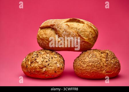 Horizontal composition of a small bread loaf placed over two round seeded buns against pink background. Modern minimalist food still life ideal for ba Stock Photo