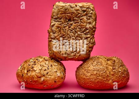 Vertical composition with a square multigrain bread balanced over two round rolls on a pink background. Conceptual food photo symbolizing structure an Stock Photo