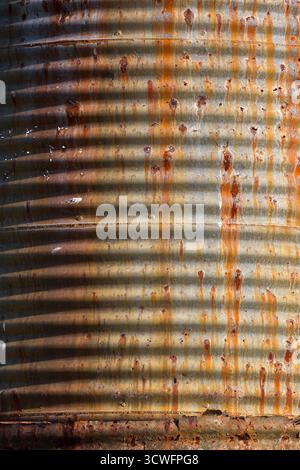 Corrugated metal surface of an old water tank, exhibiting significant rust and weathering. Stock Photo