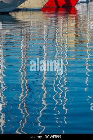 Rippling reflections of yacht masts create wavy lines on the water's surface. Stock Photo
