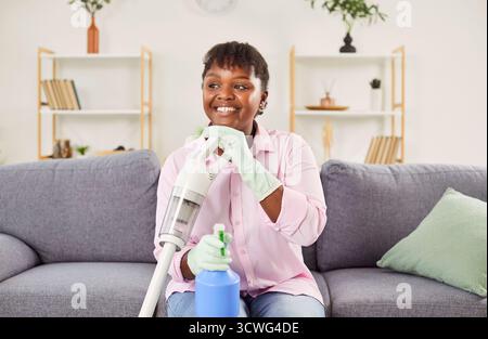 Happy middle aged african american woman sitting rest after cleaning carpet and furniture  Stock Photo