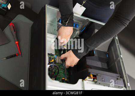 Adult male IT technician performing server hardware upgrade inside a computer rack during maintenance Stock Photo