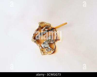 A burnt white paper with a hole in the center and dark brown burn marks around the edges. A burnt matchstick, blackened, is placed on the burnt paper. Stock Photo