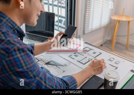 A young male architect is working with blueprints at his desk, using rulers and drawing tools to refine details. He appears focused and engaged, balan Stock Photo