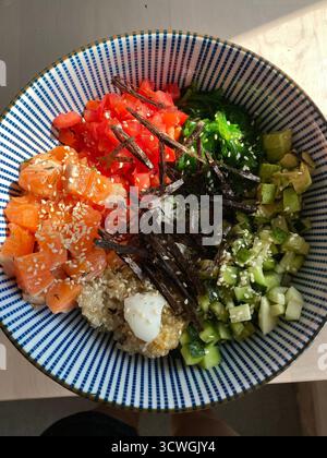 Poke bowl with salmon, cucumbers, tomatoes, seaweed, and quinoa in a striped bowl background. Mobile photo Stock Photo