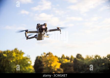 Hamburg, Germany - September 30, 2025: DJI Mini 5 Pro Lightweight Camera Drone in Flight against blue Sky over Autumn Park during Golden Hour - Wide Stock Photo