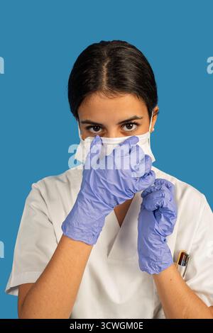 Female medical worker adjusting her face mask and wearing protective gloves, looking at camera Stock Photo