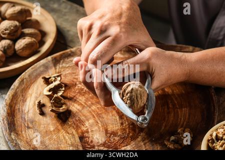 Elderly woman cracking walnuts with nutcracker on wooden board Stock Photo