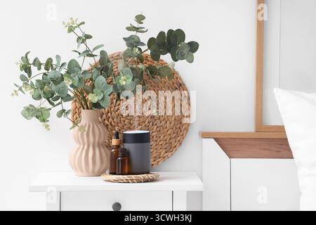 Air humidifier, essential oils and vase with eucalyptus on table in bedroom Stock Photo