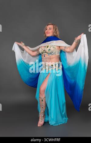 Smiling mature woman fashion model in dance stage outfit - bra top and blue maxi skirt and she is not wearing any footwear. Three quarter front view f Stock Photo