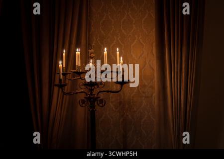Close-up of candelabra with lit candles in the manor hall. Lighted candles on floor standing candelabra in large room. Stock Photo