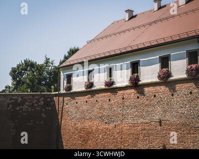 The outer façade of Stari Grad Castle in Cakovec, Croatia, with its red brick walls and white upper structure. Flower-adorned windows add charm to the Stock Photo