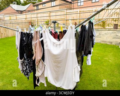 Colorful clothes hanging on an outdoor rotary washing line in a suburban backyard with a neatly fenced lawn uk Stock Photo