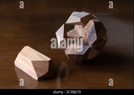 A wooden puzzle ball with one piece out of place on a wood table Stock Photo