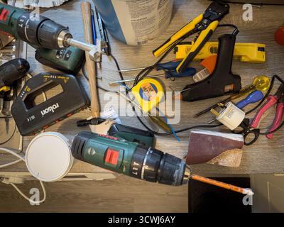 A cluttered workbench with various tools including drills, measuring tape, wire strippers, and hand tools for home improvement projects Stock Photo