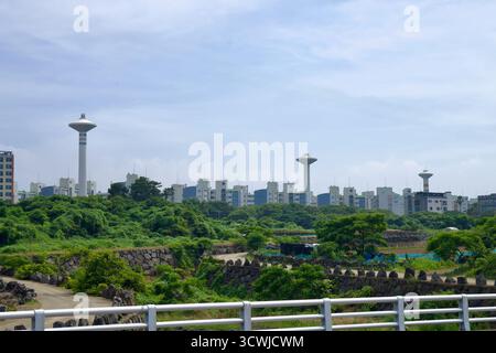 Mushroom‑shaped water towers and apartment blocks rise behind green belts and old stone walls east of Jeju Harbor, seen from the Samyang–Hwabuk coastl Stock Photo