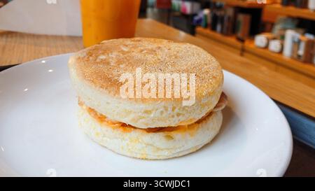 Close-up of a delicious english muffin sandwich with egg and cheese on a white plate in a cafe Stock Photo