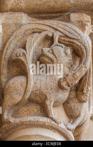 A close-up of an ancient, weathered stone capital featuring a detailed carving of a mythical beast with wings and a human head, showcasing intricate m Stock Photo