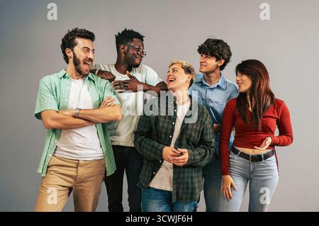 A cheerful multi-ethnic group of five young friends in casual clothing laughing and having a positive interaction together while standing in a studio Stock Photo