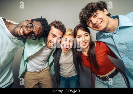A dynamic low angle point of view shot of a cheerful multi-ethnic group of young friends huddled together, smiling and laughing directly at the camera Stock Photo