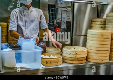 Kuala Lumpur, Malaysia - August 02, 2024: Asian chef is preparing dim sum using bamboo steamer in a busy kitchen environment. Stock Photo