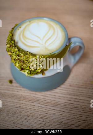 Matcha latte with heart-shaped latte art and crushed pistachio rim in blue ceramic mug Stock Photo