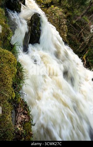 Cascading waterfall flowing over mossy rocks in Lake District countryside Stock Photo