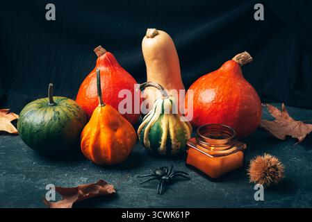 Various pumpkins, fallen leaves, candle and spider on black background. Halloween concept. Closeup. Stock Photo