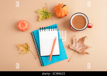 Autumn flat lay with coffee cup, notebooks, pen, pumpkins, leaves and candle on beige background. Cozy seasonal workspace concept. Top view, mockup. Stock Photo