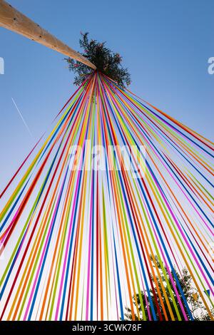 Vibrant ribbons radiate from a tall decorated pole during a lively festival in Tarvisio, Italy. Stock Photo