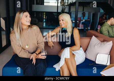 Two women, one young and one mature, sitting on a couch in an office, smiling and chatting, creating a positive and friendly atmosphere in a professio Stock Photo