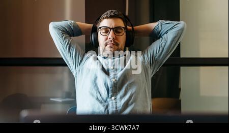 A man relaxes with headphones in a stylish modern office environment, exuding comfort and professionalism. This represents a moment of calmness amidst Stock Photo