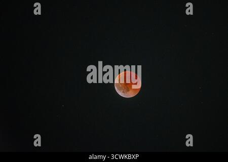 The magnificent Blood Moon glows with an intense red and orange hue during a total lunar eclipse, set against a vast, dark sky sprinkled with distant Stock Photo