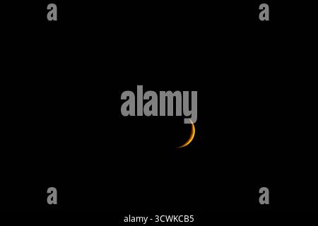 A delicate golden sliver of a crescent moon glowing brightly against the pitch-black canvas of the deep night sky. Minimalist astrophotography with am Stock Photo