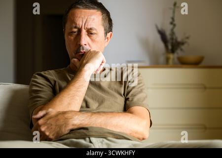 Pensive middle-aged man sitting indoors, thoughtful and serious expression, resting his chin on hand in contemplation. Selective focus. Stock Photo