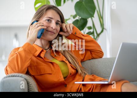 Middle-aged woman happily talking on phone having nice conversation during break from laptop work  Stock Photo