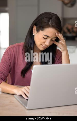 Tired Latin woman touching head at home workplace table Stock Photo