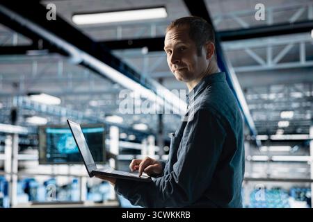 Cheerful server farm worker uses specialized hardware to accelerate complex AI calculations. Portrait of smiling engineer in data center providing computing resources and storage to enable AI training Stock Photo