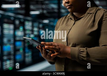 Close up of system administrator using tablet in data center to track metrics of gear used to host websites. Server room IT specialist upgrading capacity of storage rigs running companies databases Stock Photo