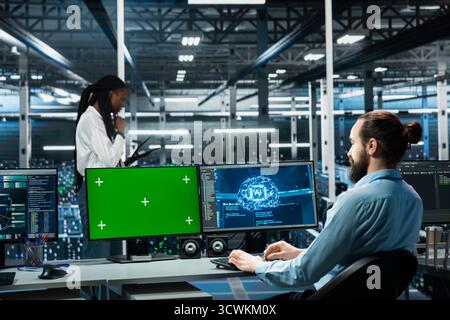 Data center technician monitoring AI systems using green screen mockup PC. Server room IT specialist using chroma key isolated computer, enhancing artificial intelligence performance Stock Photo