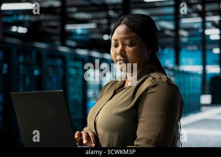 Data center programmer using laptop to optimize network infrastructure, planning capacity. IT expert managing server farm resources with notebook for improved reliability and uptime Stock Photo