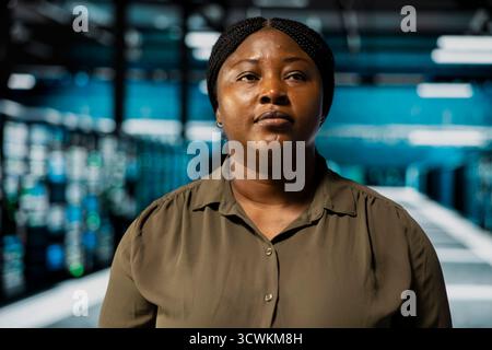 Close up of technician doing maintenance in data center with setup helping companies stay connected. African american worker walks in server farm with machines blinking lights showing system activity Stock Photo