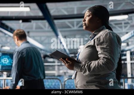 Server room infrastructure engineers scripting automated workflows using software on tablet. Teamworking data center programmers running predictive maintenance scans using device Stock Photo